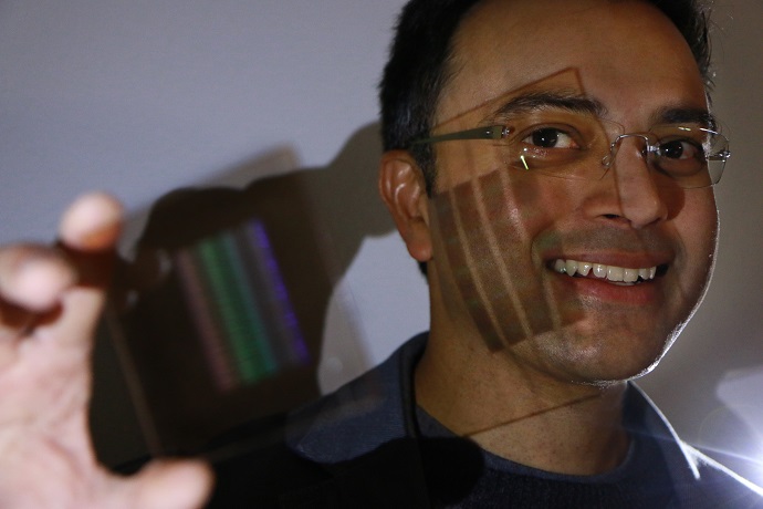 University of Utah electrical and computer engineering professor Rajesh Menon holds up the prototype of the first flat thin camera lens that he and his team developed