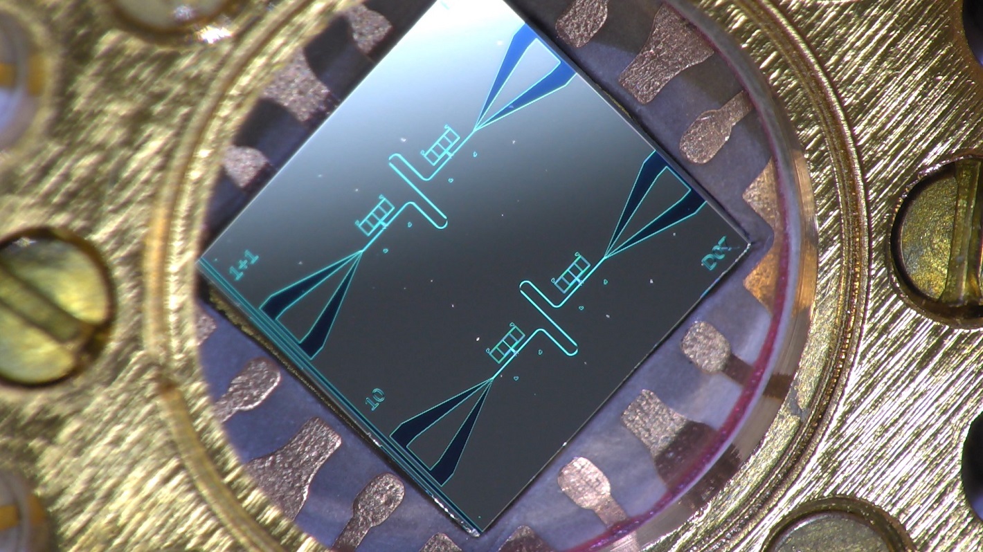 Photo of a centimeter-sized silicon chip, which has two parallel superconducting resonators and quantum-circuit refrigerators connected to them