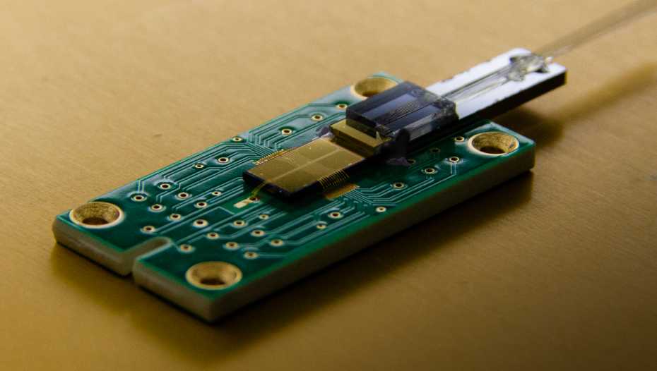 The ion-​trap chip with integrated waveguides. The laser light is fed into the chip via the optical fibres on the right