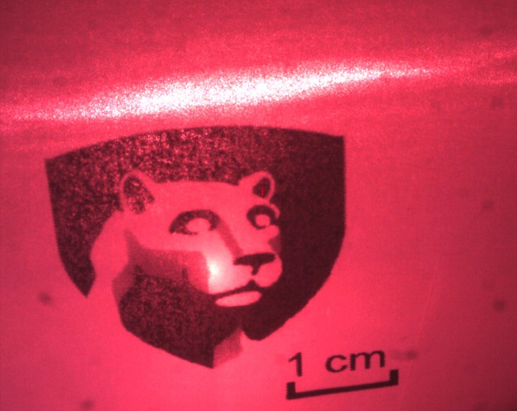 A red laser beam shines on a card bearing a replica of Penn State's academic logo