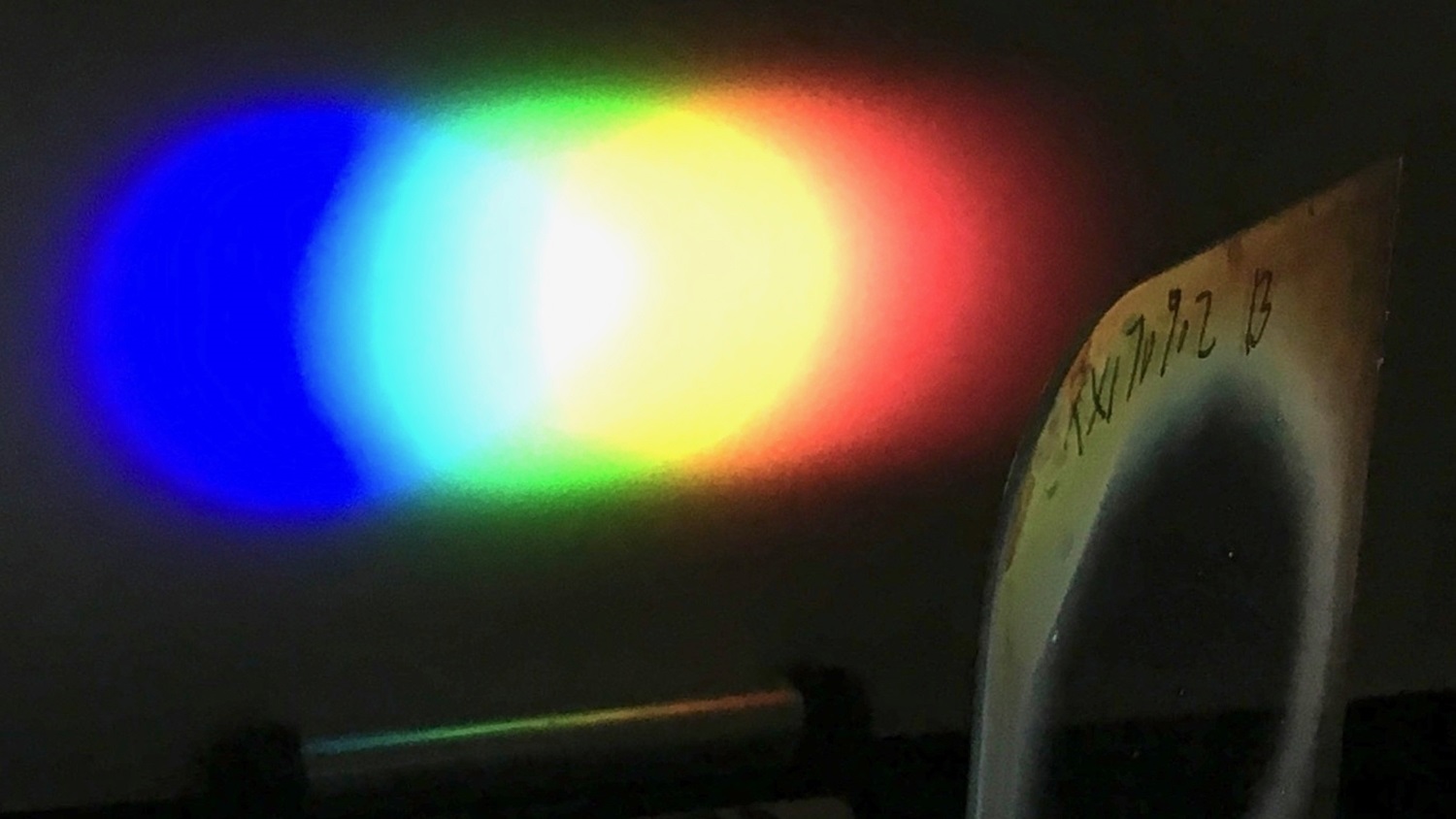 A one-inch diameter Bragg polarization grating diffracts white light from an LED flashlight onto a screen placed nearby