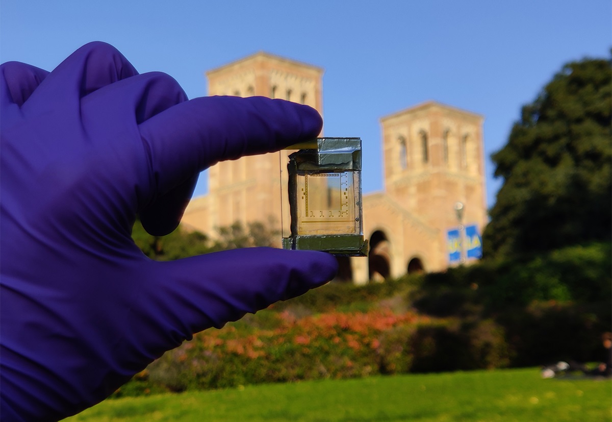 Gloved hand holding up small device with Royce Hall in the background